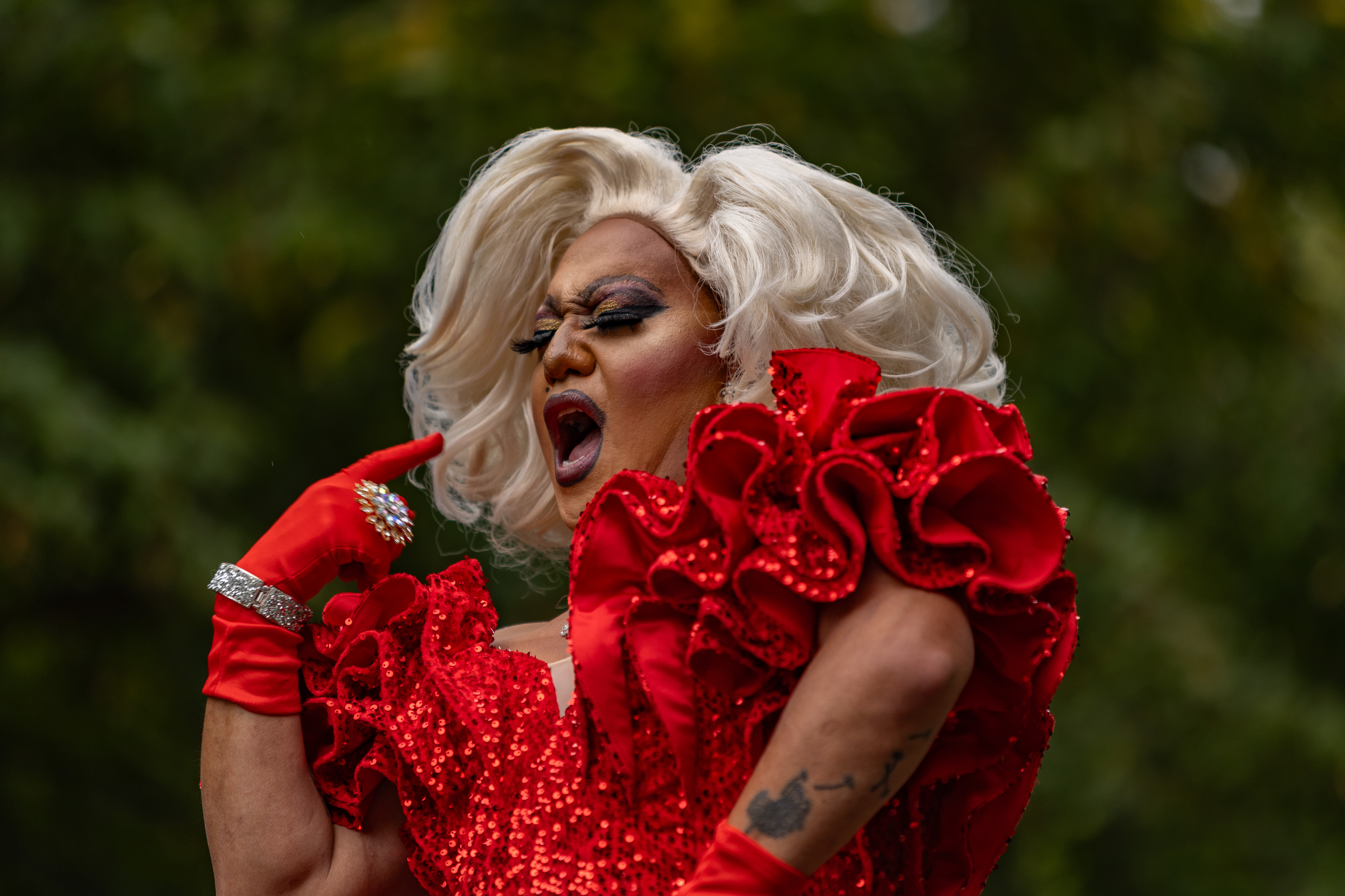 Drag performer in a ruffled red sequin gown and platinum wig mid-performance outdoors