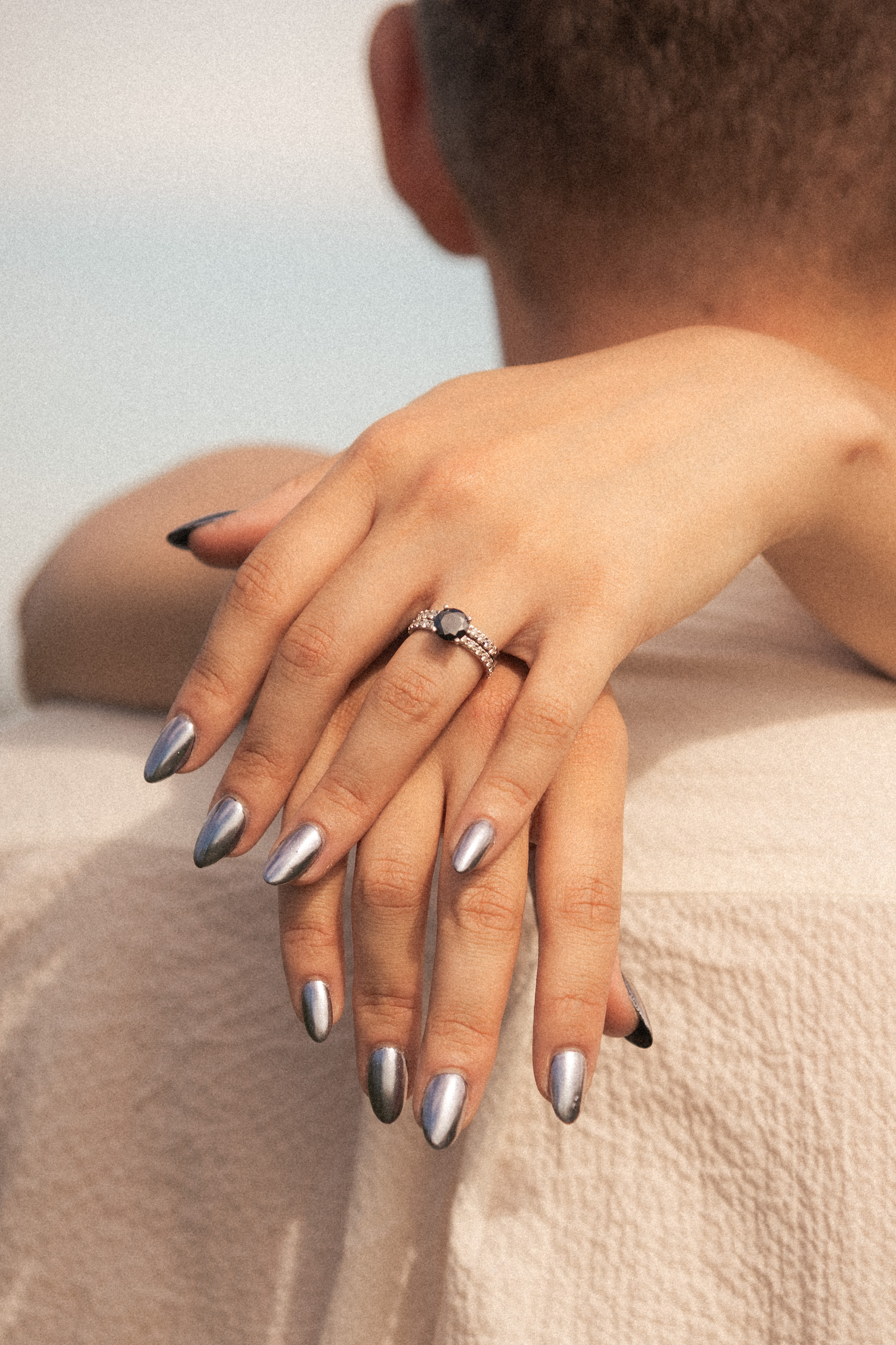 Close-up of a bride's hand with an engagement ring and silver nails resting on the groom's shoulder