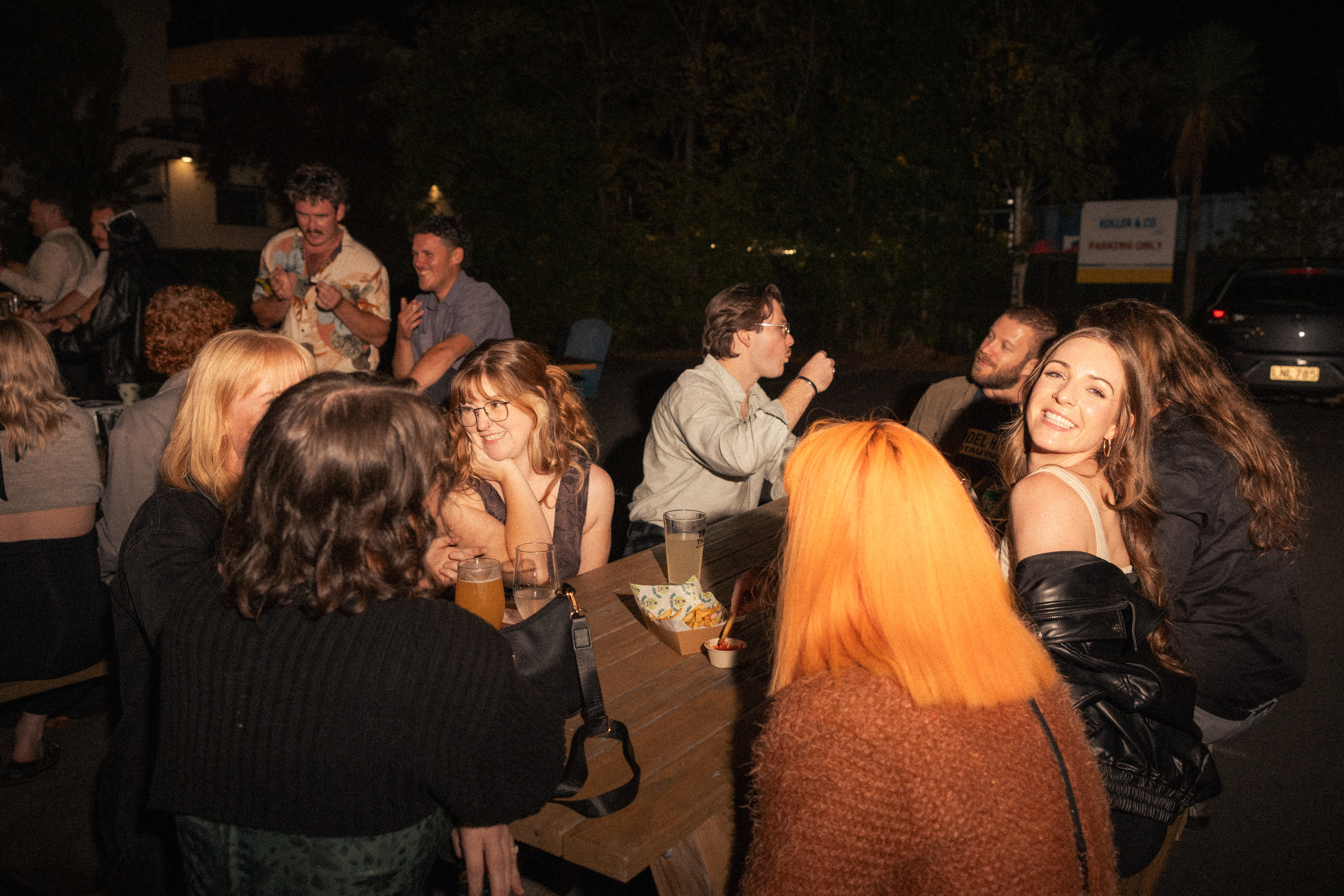 Friends laughing together around outdoor tables at a relaxed night-time celebration