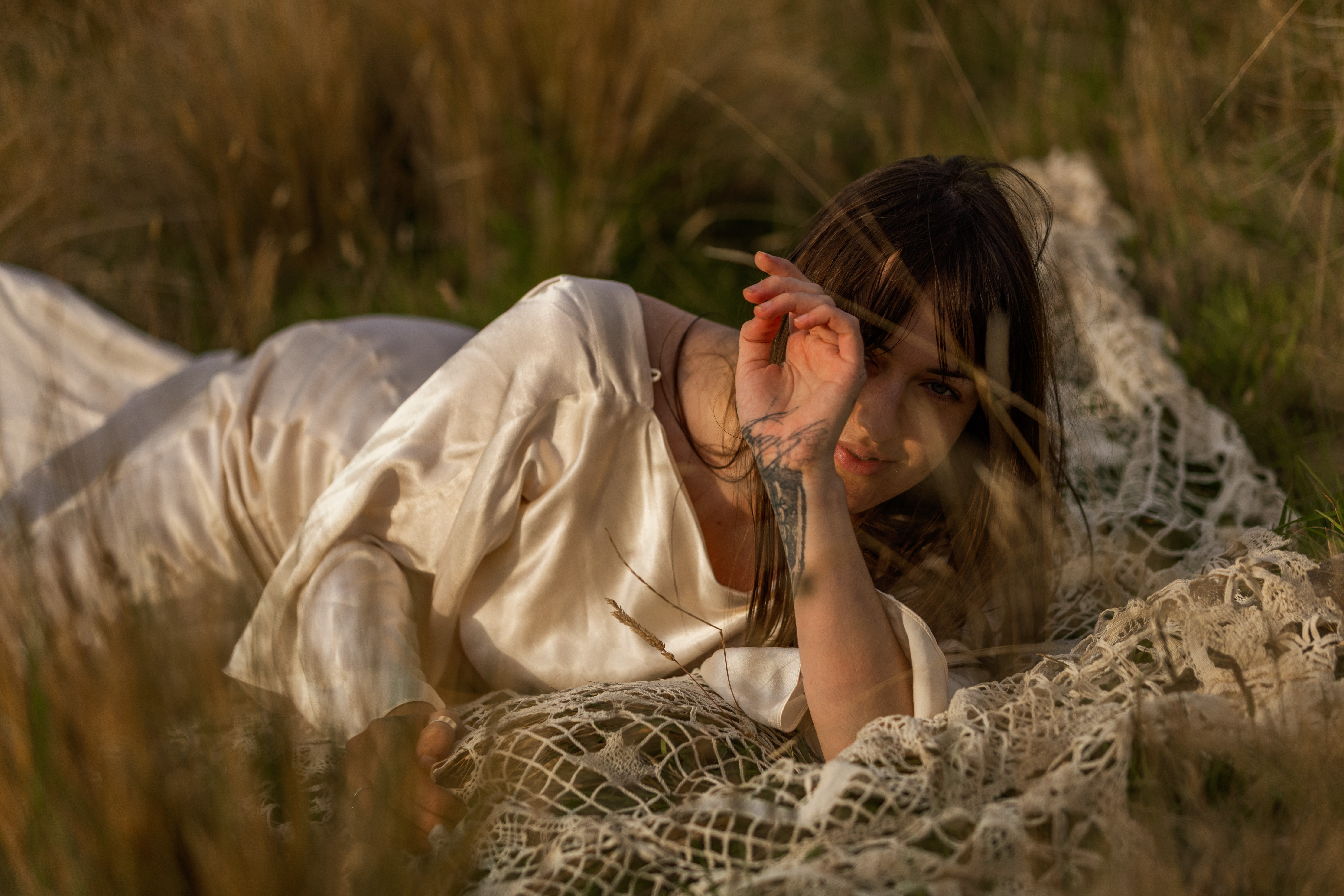 Woman in cream silk reclining on a vintage lace blanket in golden-hour grass